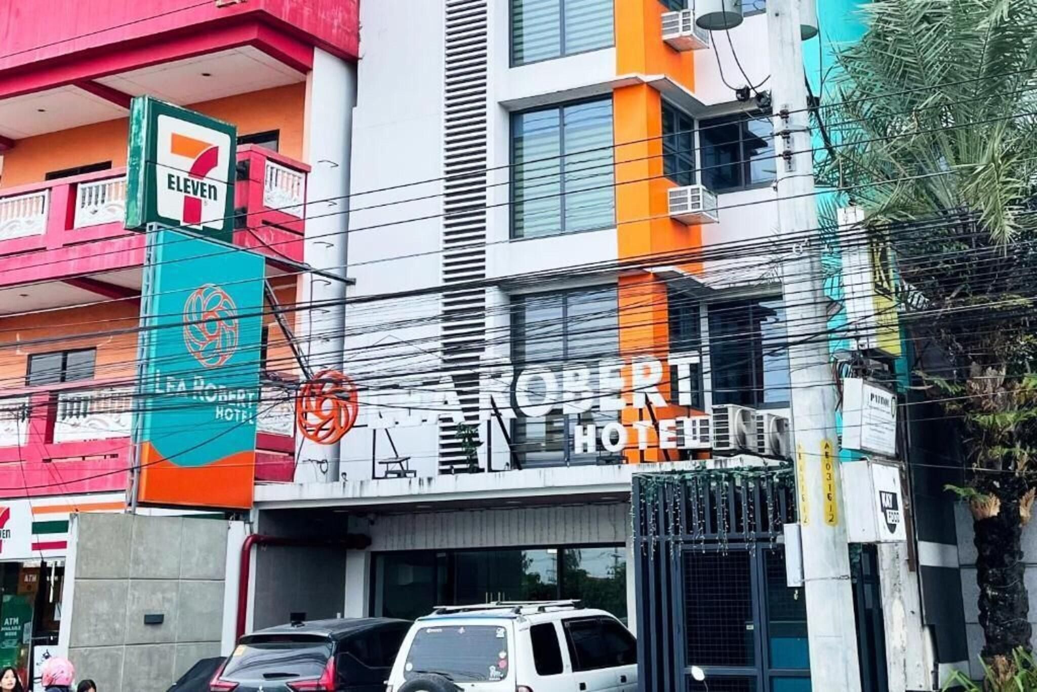A hotel with a prominent sign, multiple floors, and a parking area with cars.