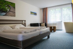 Ein Hotelzimmer mit Bett, Stuhl, kleinem Tisch und einem Fenster mit Vorhängen.