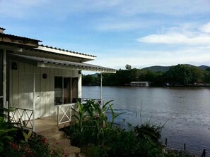 A white building with a covered porch and a view of a lake. - Hadsaisuay Resort And Homestay (Kanchanaburi)