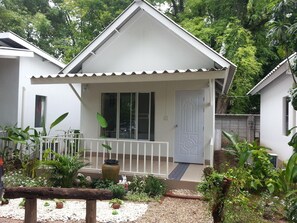 A white house with a covered porch, a door, and a small garden area with plants and gravel. - Hadsaisuay Resort And Homestay (Kanchanaburi)