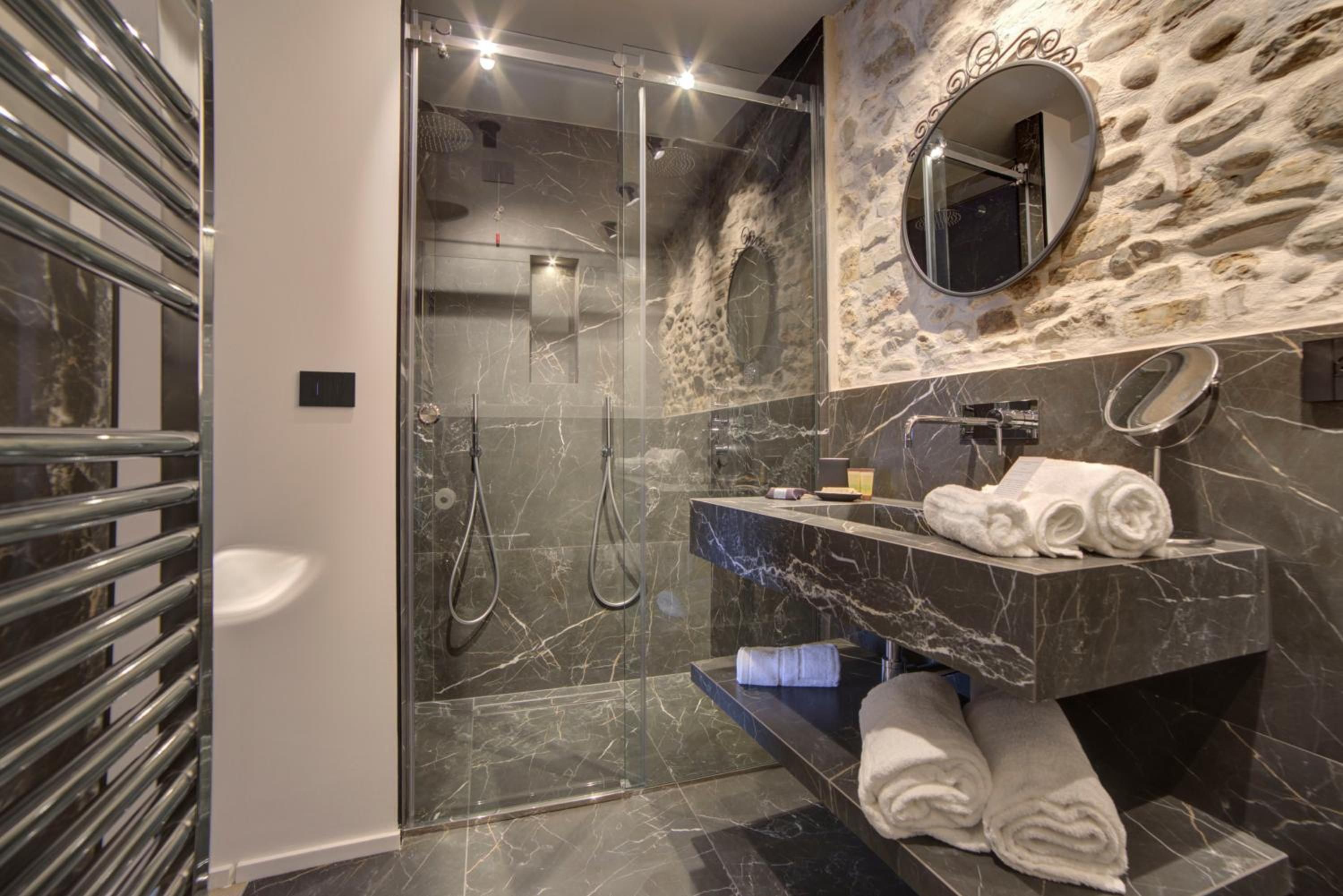 Ein modernes Badezimmer mit einer gläsernen Duschkabine, Marmor-Waschtischen, einem integrierten Waschbecken und einem Spiegel mit dekorativem Rahmen.