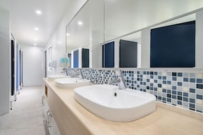 A modern bathroom with three sinks, a hand dryer, and a tiled backsplash.