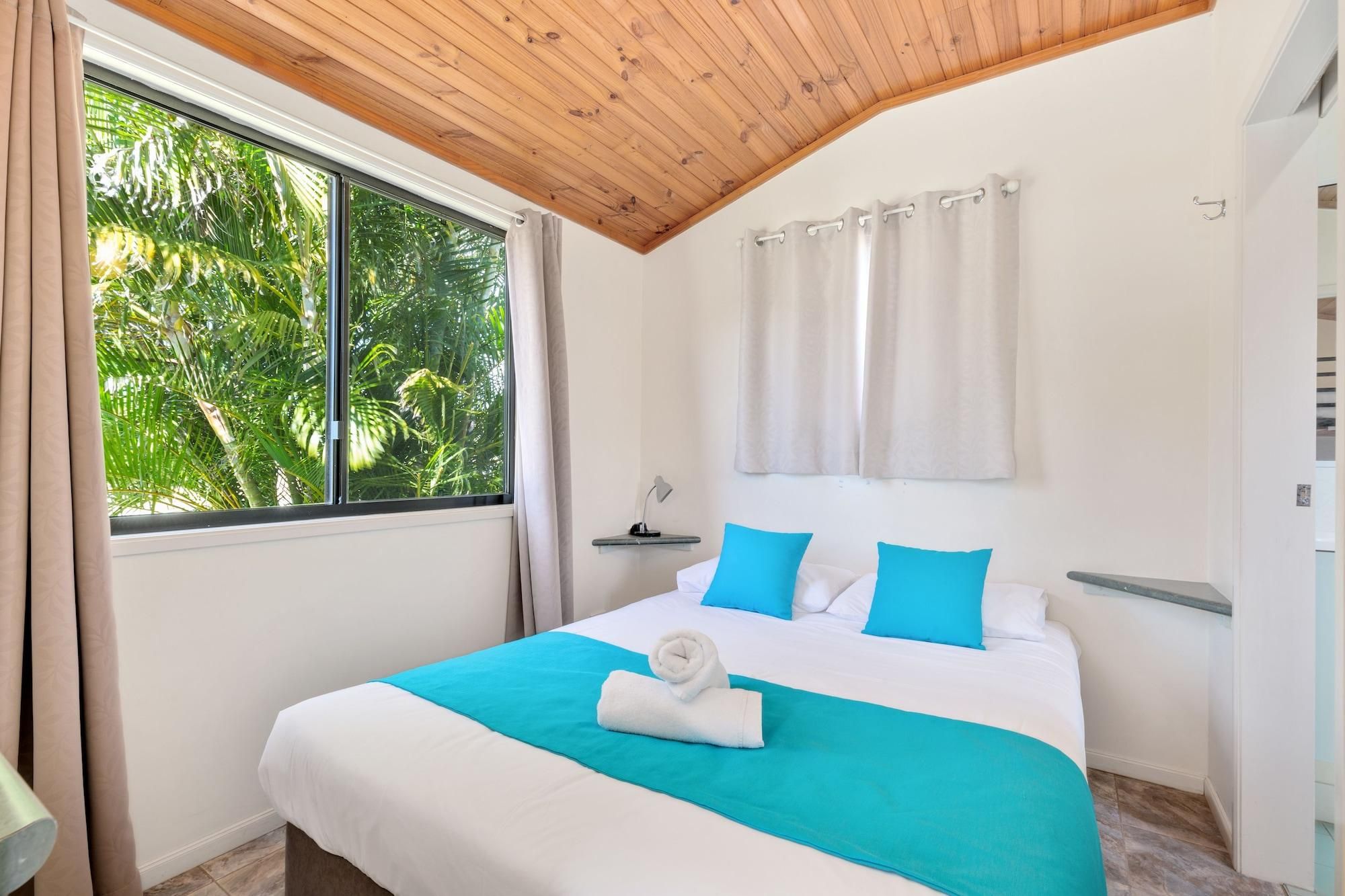 Habitación de hotel con una cama grande, techo de madera, ventana con cortinas y vistas a zonas verdes.