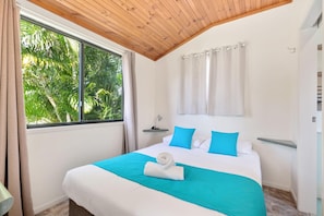 A hotel room with a large bed, a wooden ceiling, a window with curtains, and a view of greenery outside.