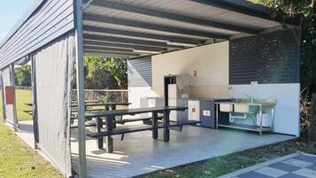 Un espacio al aire libre cubierto con mesas de picnic, un lavamanos y un refrigerador.