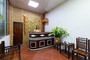 A reception area with a wooden desk, a chair, a potted plant, and a traditional decorative wall. - Mh Cherish Homestay (Hoa Lu)