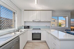 A modern kitchen with white cabinetry, a Bosch dishwasher, a built-in oven, and a window with a view of a residential area. - Whitecaps at Kings Beach (Kings Beach)