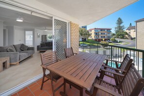 A balcony with a wooden table and chairs, a grey sofa, and a TV in the background. - Whitecaps at Kings Beach (Kings Beach)