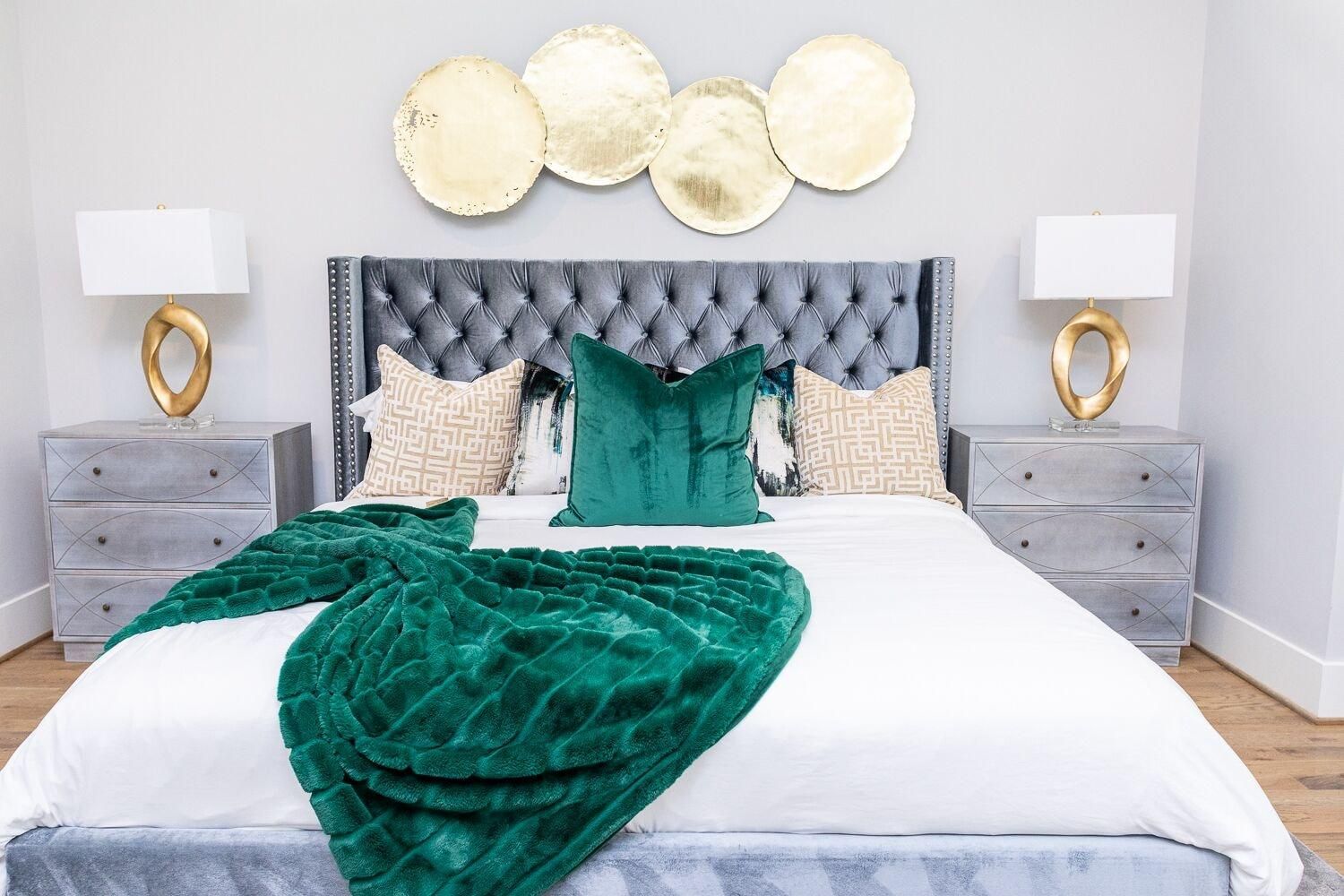 A bed with a tufted headboard, multiple pillows, a green throw blanket, and two bedside tables with lamps.