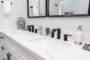 A bathroom with a white marble countertop, two black faucets, a glass soap dispenser, and a mirror above the sink.