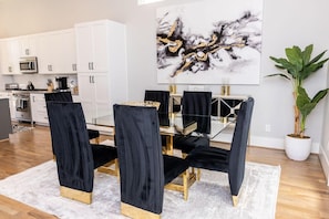 A modern dining area with a glass table and black velvet chairs, white cabinetry, and a large abstract painting.