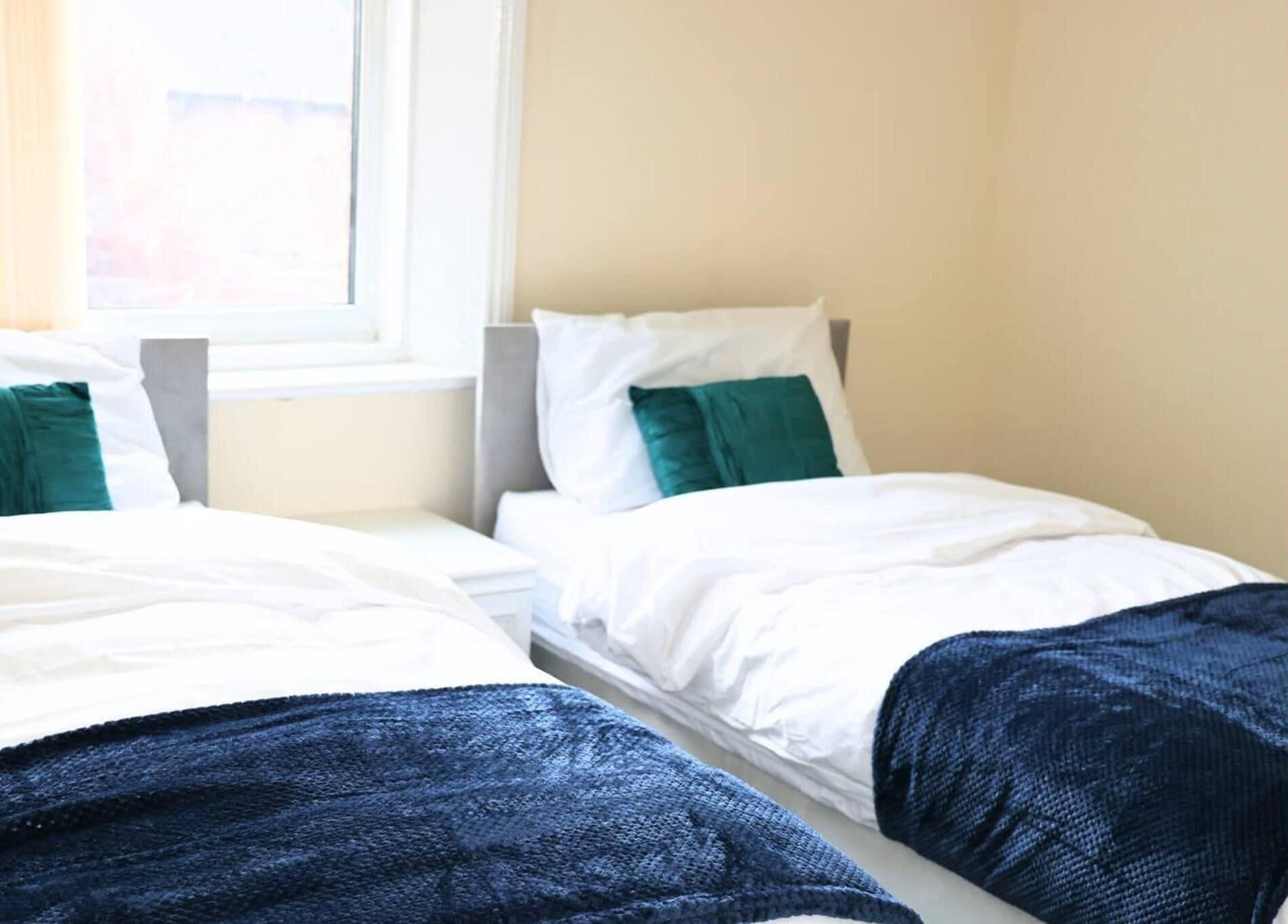 A hotel room with two single beds, each with white bedding and green pillows.
