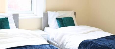 A hotel room with two single beds, each with white bedding and green pillows.