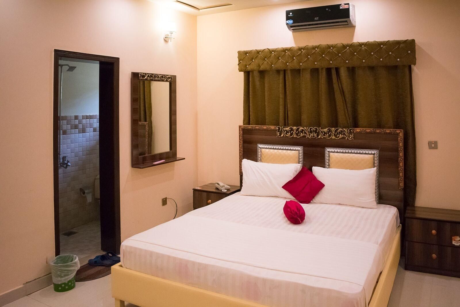 A hotel room with a bed, a bedside table with a phone, a mirror, and a wall-mounted air conditioner.