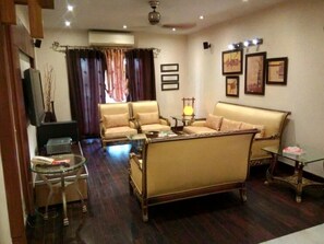 A living room with a sofa, armchairs, a glass coffee table, and a television. - Hotel Days Inn Two (Lahore)