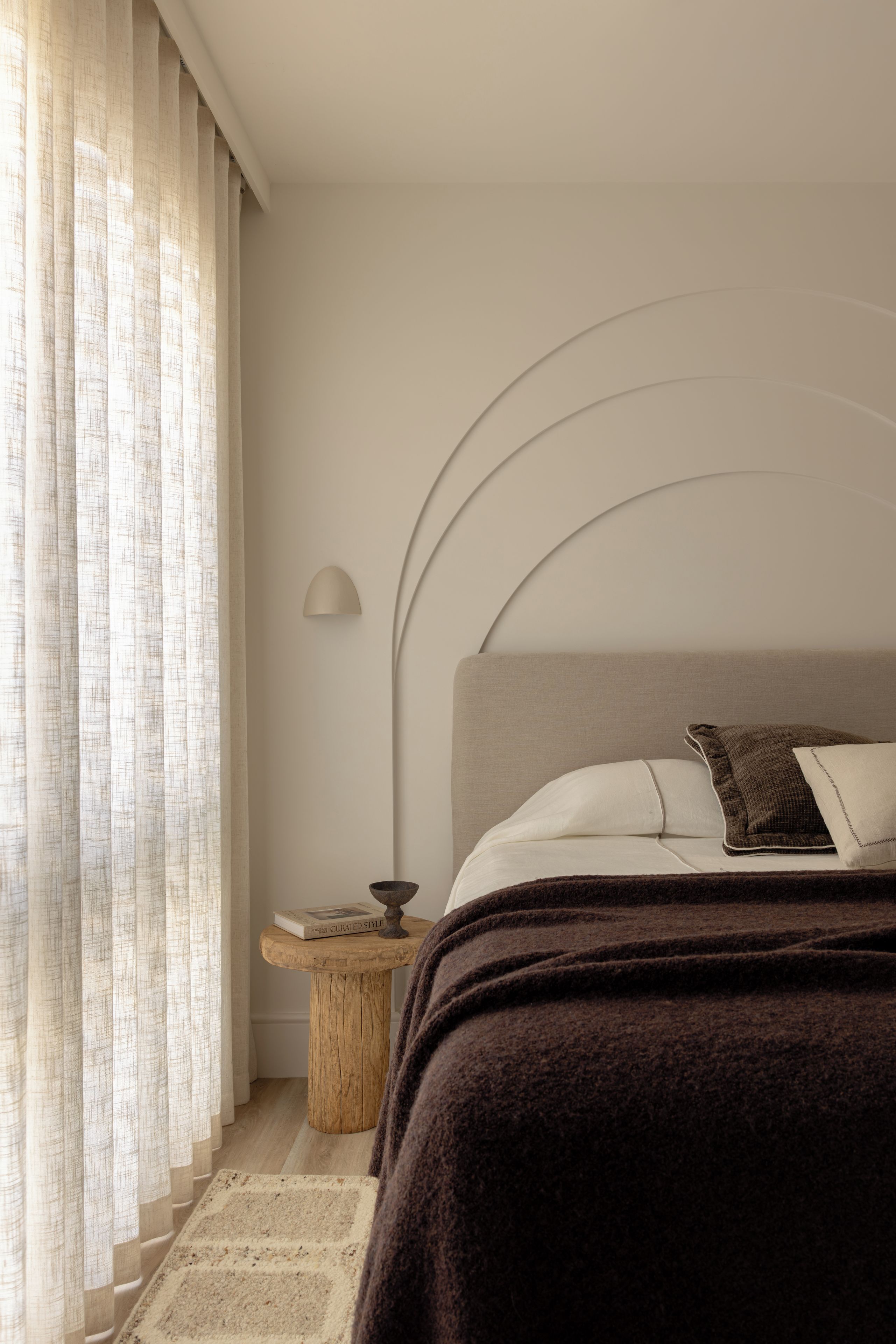 A bedroom with a bed, a bedside table, a lamp, and a window with curtains.