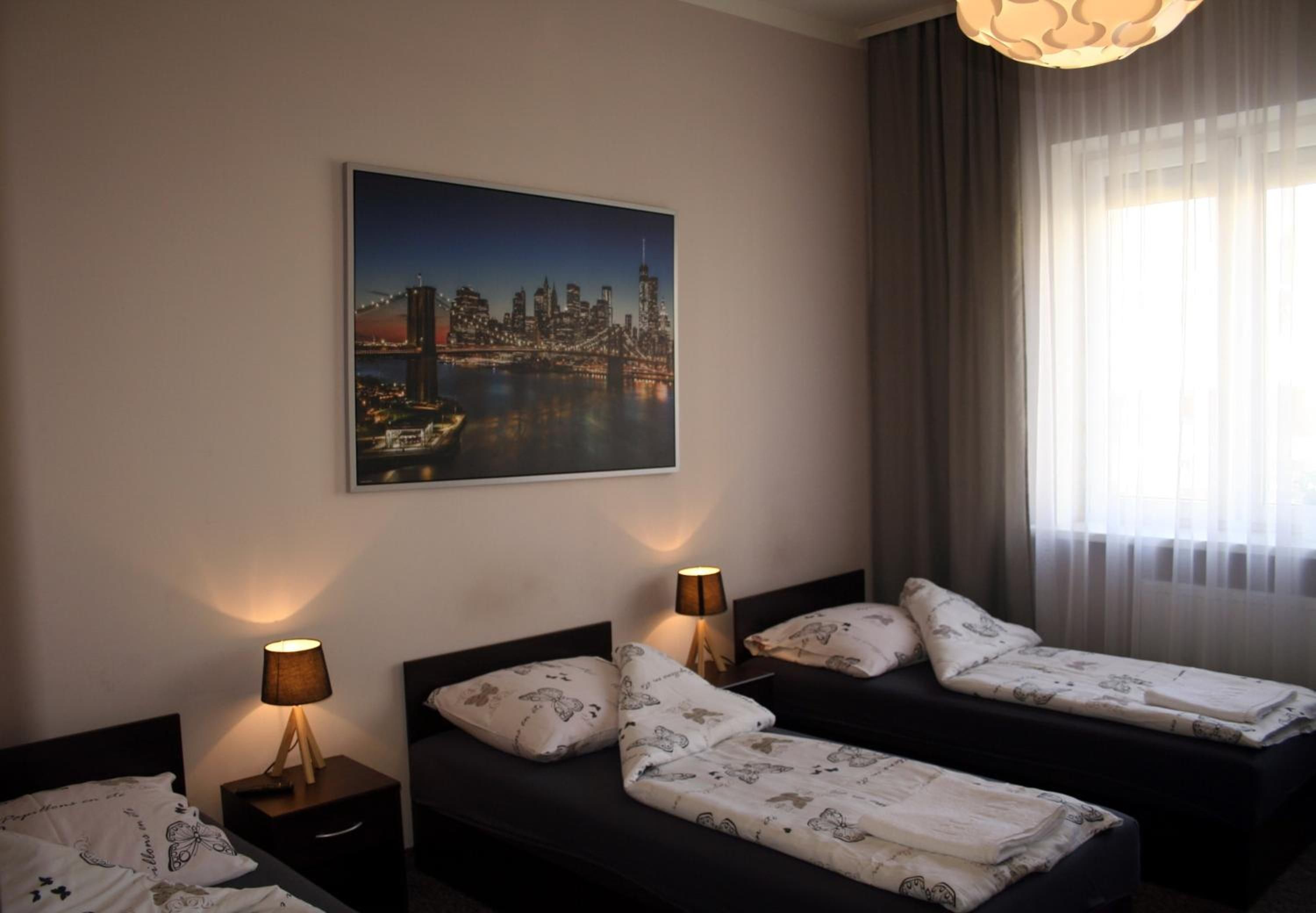 A hotel room with two beds, a cityscape painting on the wall, and a window with curtains.