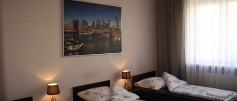 A hotel room with two beds, a cityscape painting on the wall, and a window with curtains.