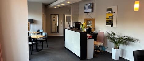 Un vestíbulo de hotel con mostrador de recepción, zona de estar y una televisión montada en la pared.