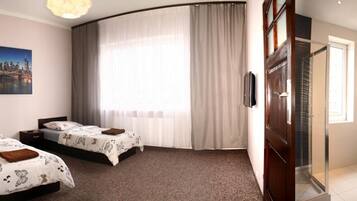 Una habitación de hotel con dos camas, un ventanal con cortinas, un cuadro de un paisaje urbano y un baño con inodoro y lavabo.
