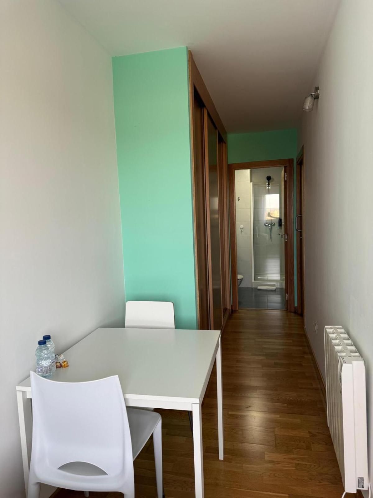 A narrow hallway with a white table and chairs, a radiator, and a door leading to a bathroom.
