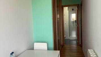 A narrow hallway with a white table and chairs, a radiator, and a door leading to a bathroom.