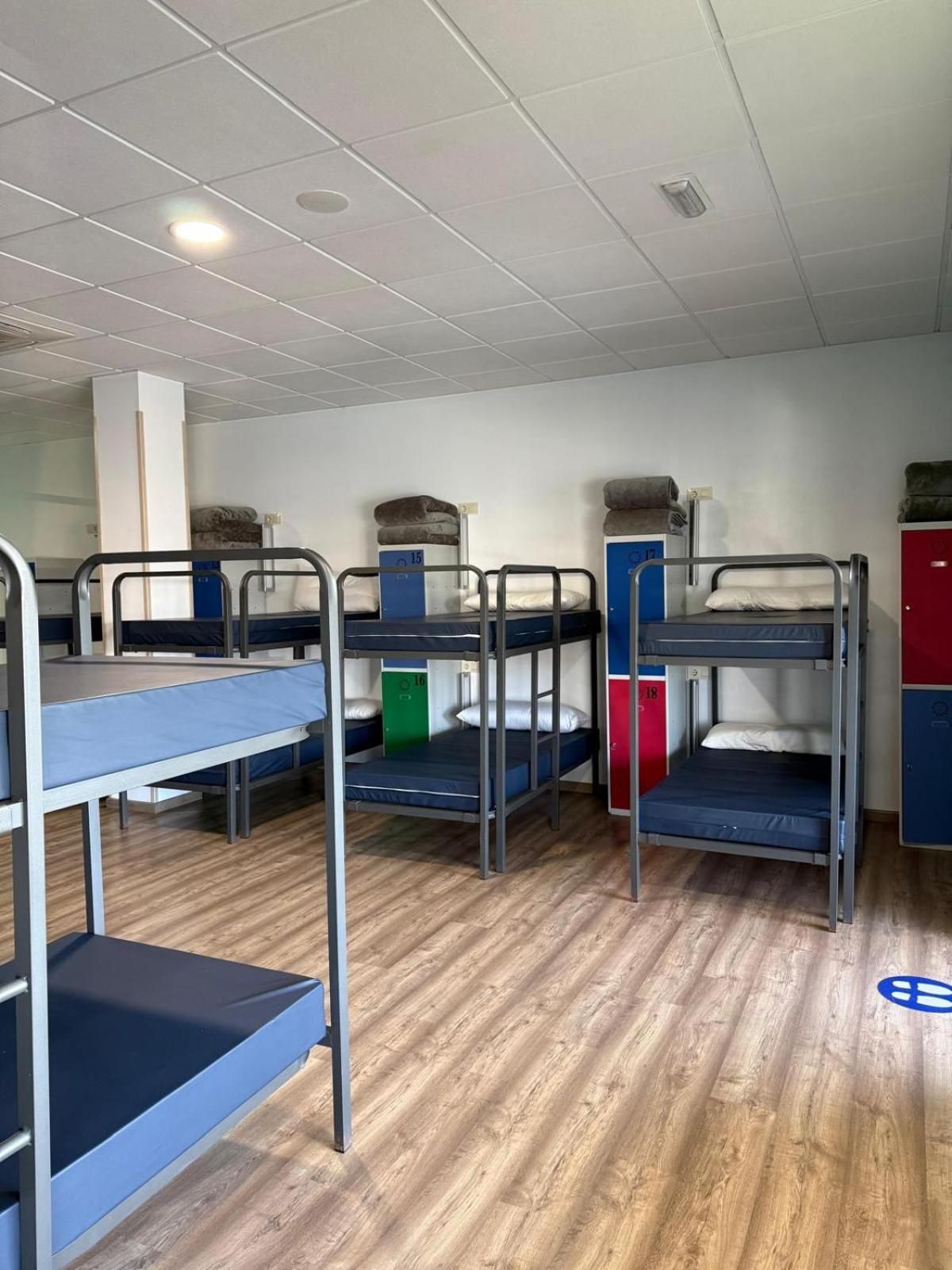 A dormitory room with bunk beds, wooden flooring, and lockers.
