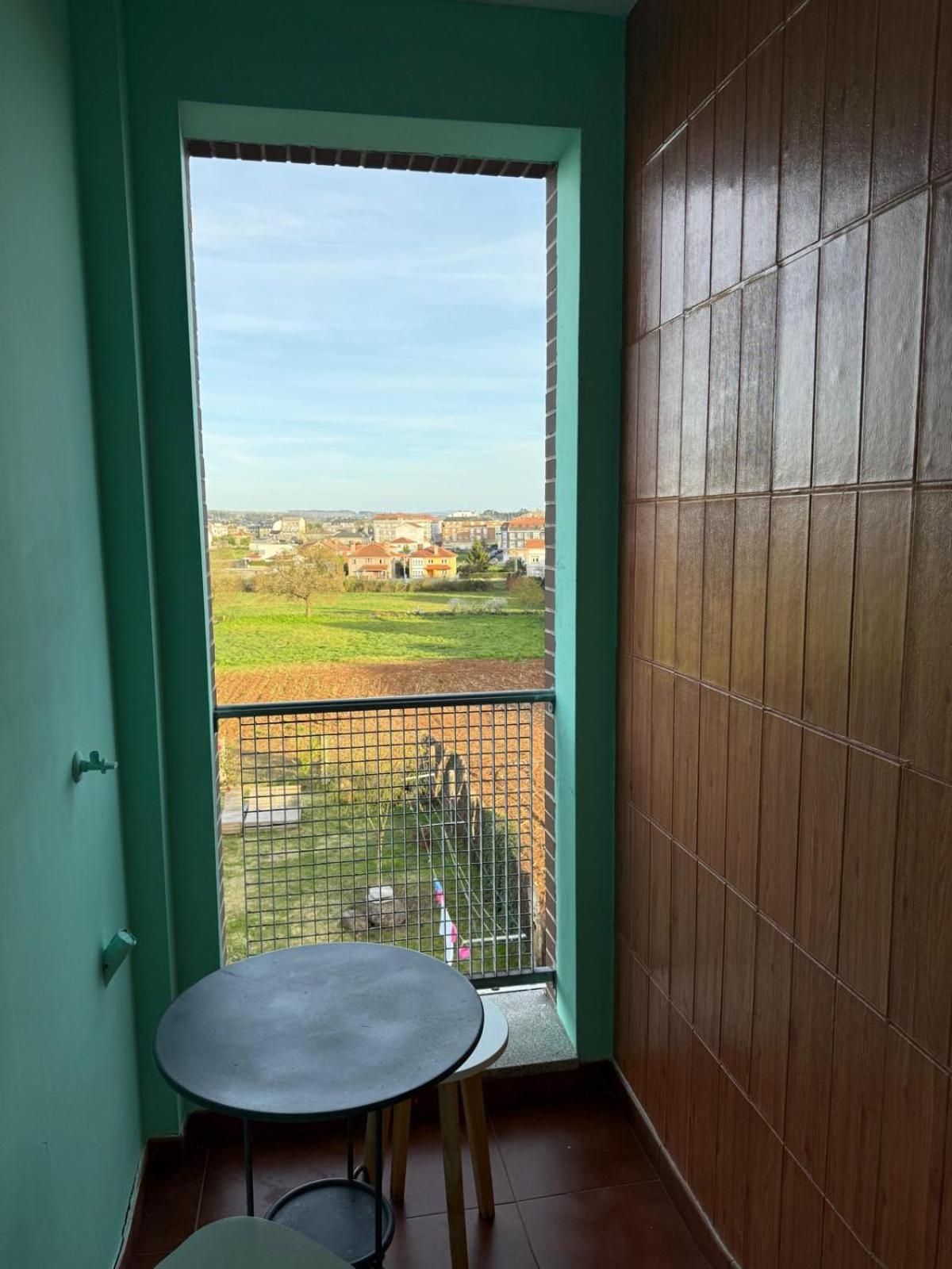 A balcony with a view of a residential area, a small table, and a chair.