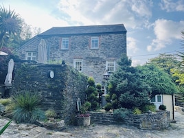 A stone building with a sloped roof, multiple windows, and a garden with various plants and a small fountain.