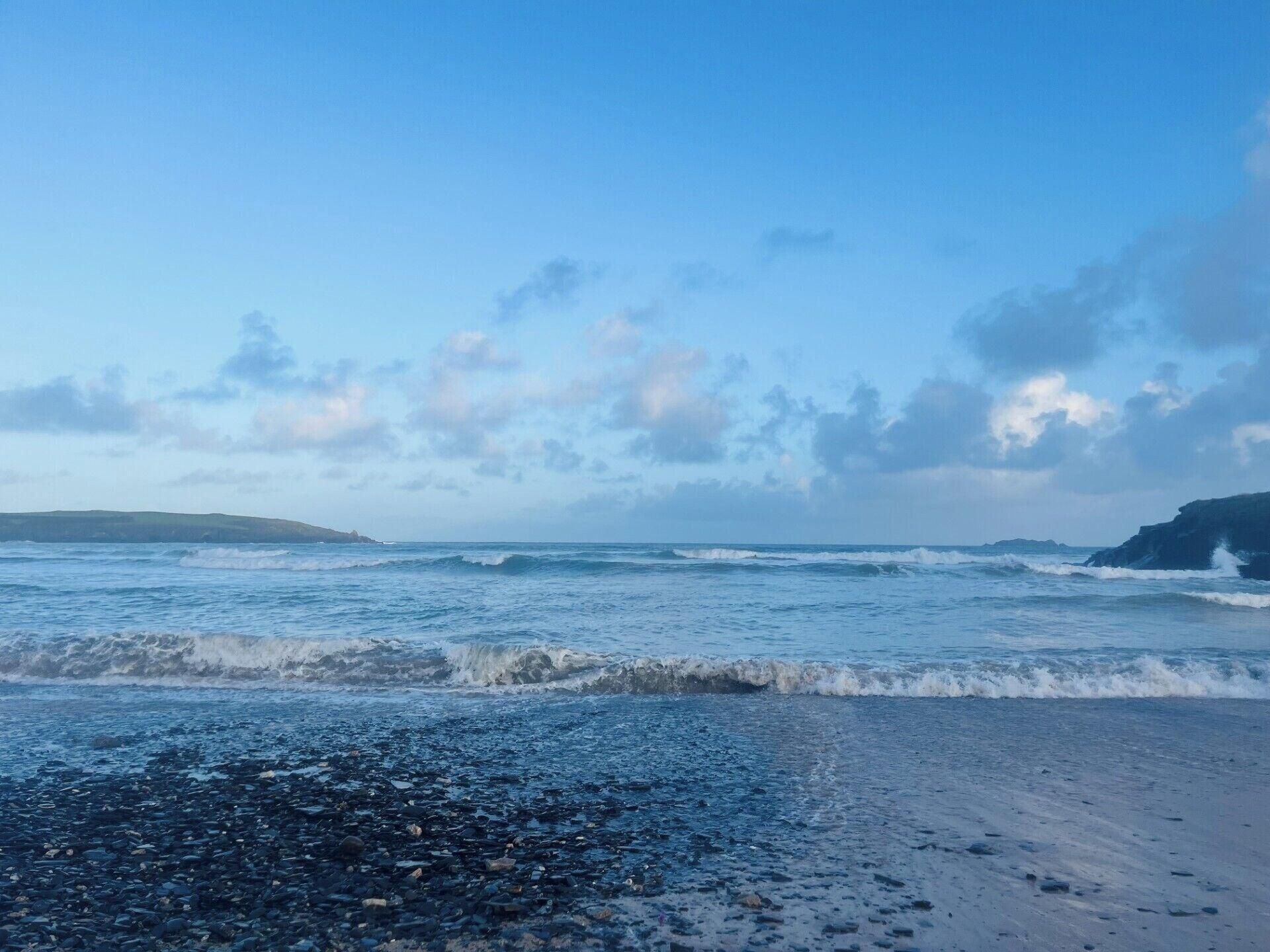 A beach with waves, pebbles, and a clear sky.