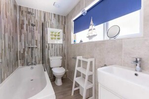 A bathroom with a bathtub, toilet, and sink, featuring a modern design with a patterned wall and a window with a view.