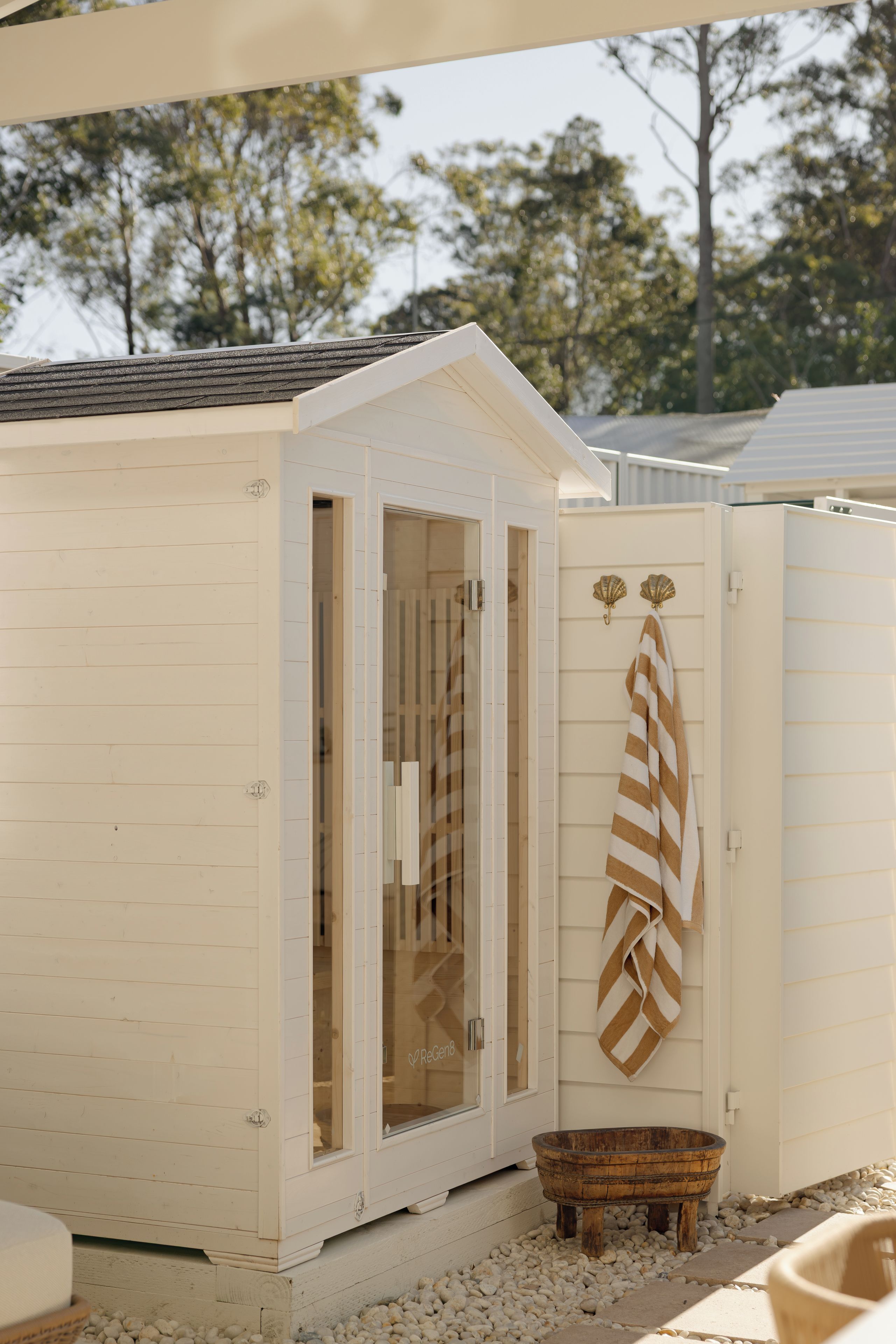 A white wooden cabin with a glass door, a wooden bucket, and a towel hanging on the wall.