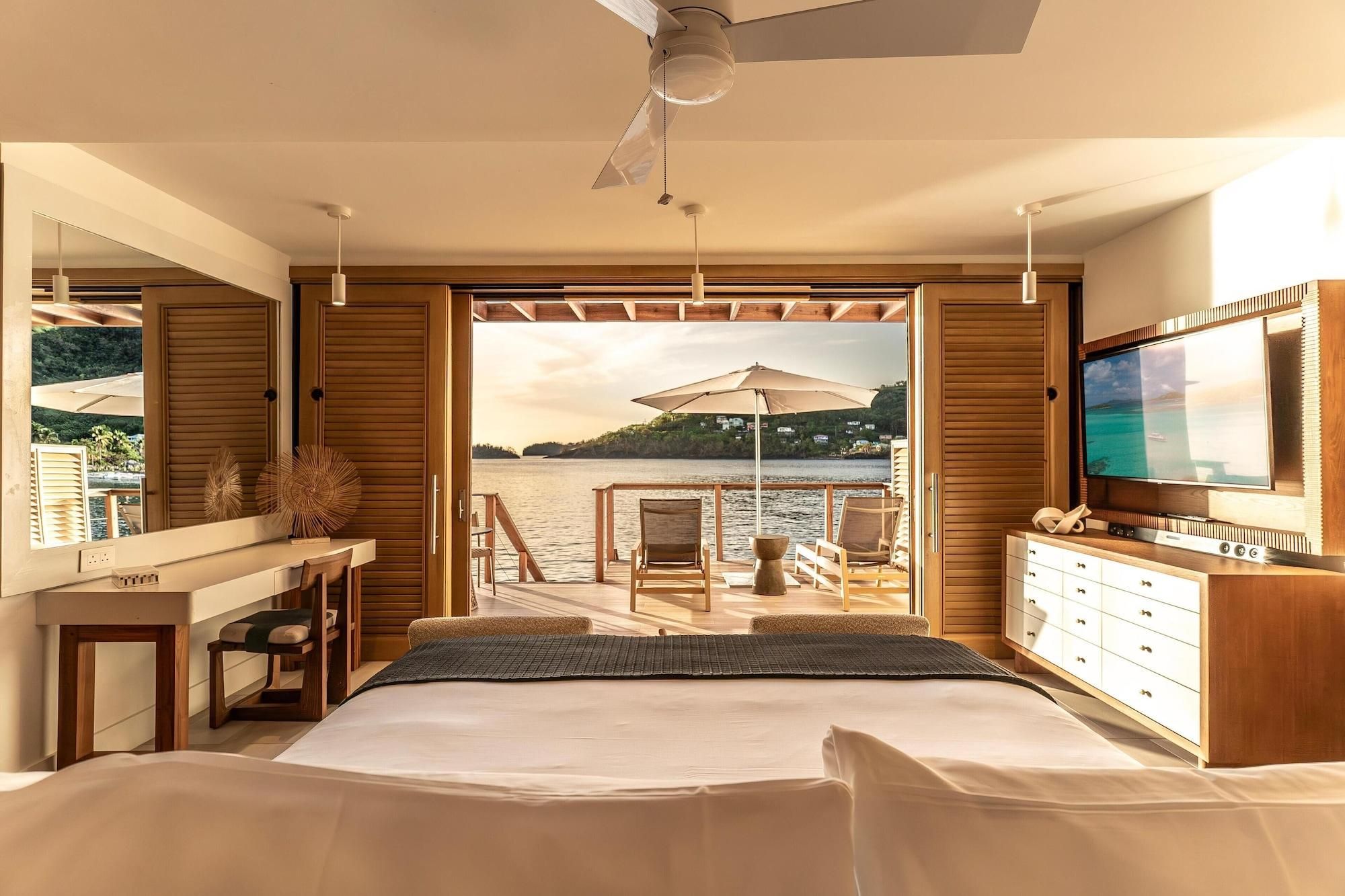 Een slaapkamer met een bed, een televisie, een bureau en uitzicht op een wateroppervlak.