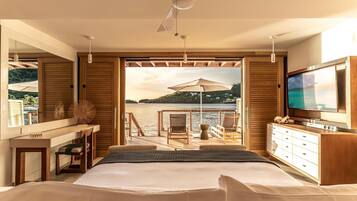 Een slaapkamer met een bed, een televisie, een bureau en uitzicht op een wateroppervlak.