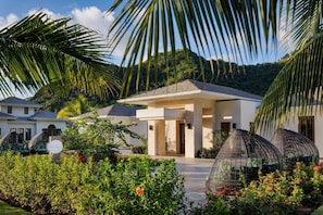 Uma villa moderna com alpendre coberto, cercada por vegetação exuberante e montanhas ao fundo.