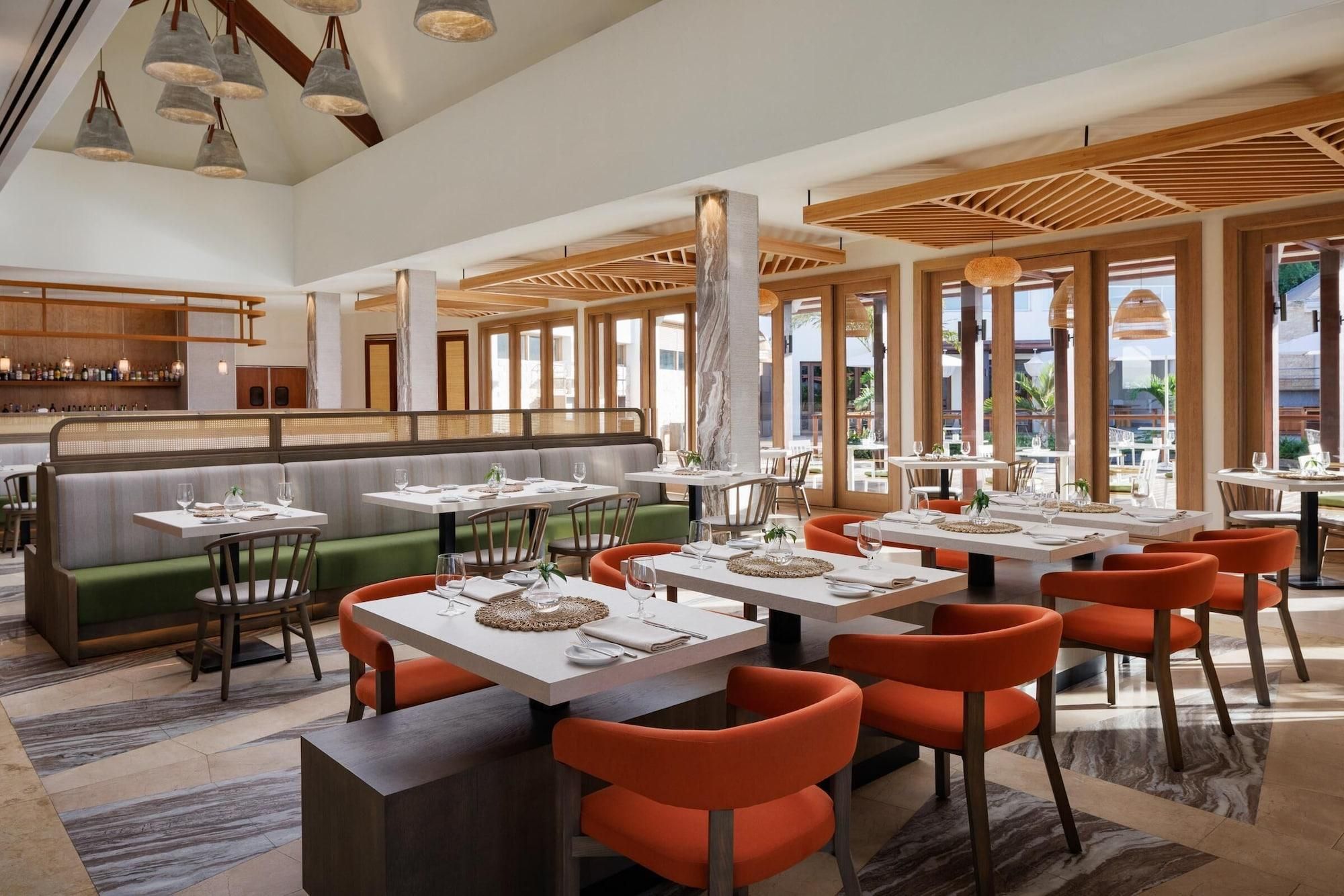 Een restaurant met hoge plafonds, grote ramen en diverse zithoeken, waaronder zitbanken en tafels.