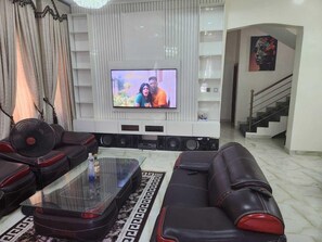A living room with a flat-screen TV mounted on the wall, leather sofas, a glass coffee table, and a patterned rug. - Impeccable 4 Bed House In Lagos Nigeria (Lekki)