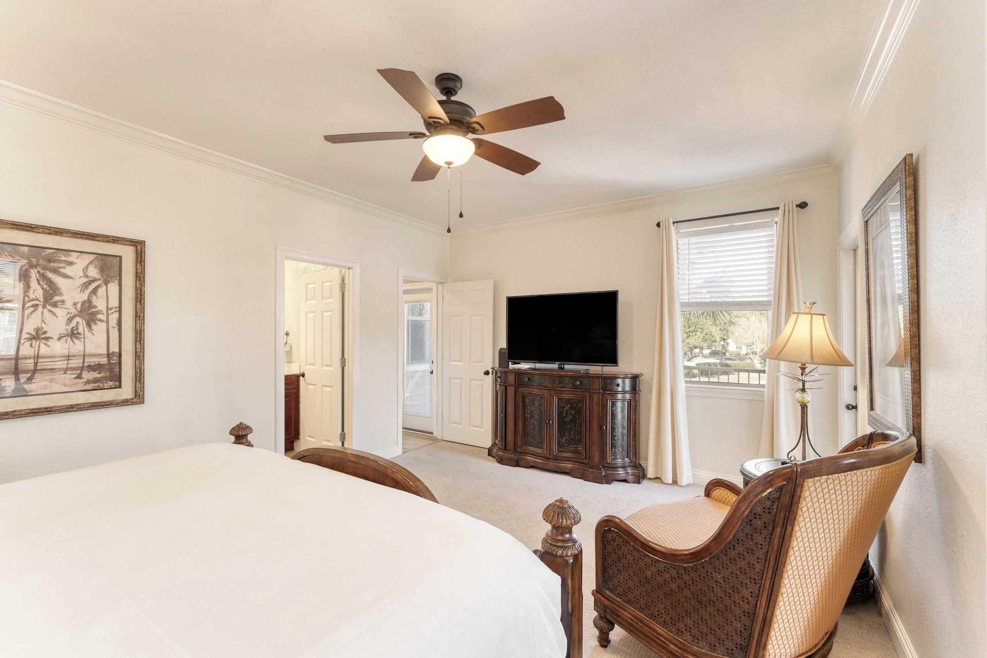 A bedroom with a bed, a television, a ceiling fan, and a lamp.