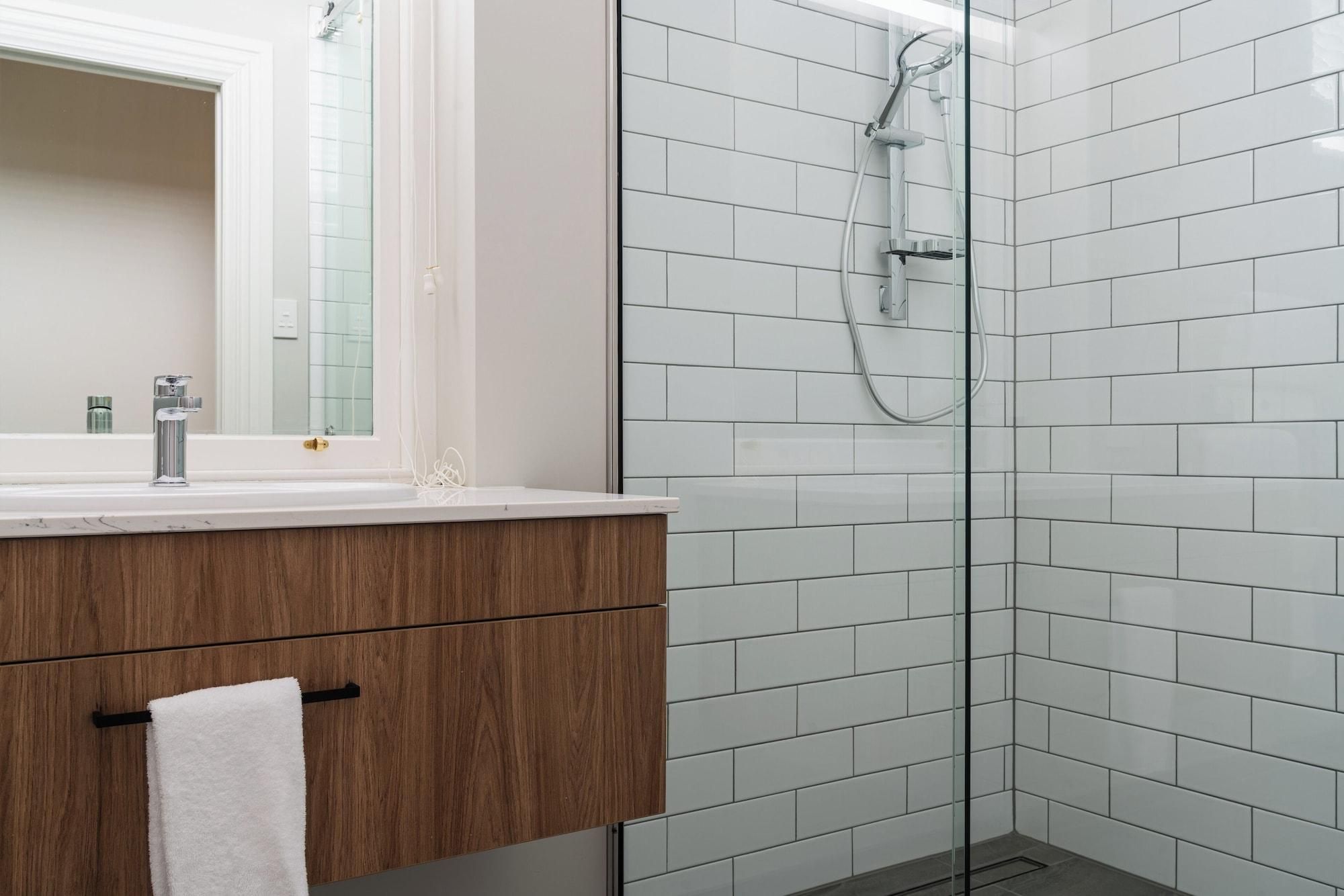 Un baño moderno con cabina de ducha de vidrio, tocador de madera y pared con azulejos blancos.
