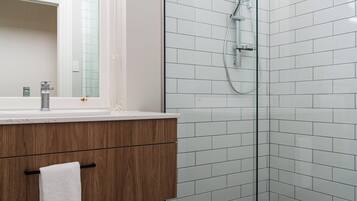 Un baño moderno con cabina de ducha de vidrio, tocador de madera y pared con azulejos blancos.