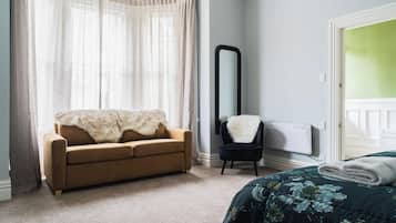 Un dormitorio con un sofá color beige, una silla negra, un espejo grande y una cama con edredón floral.