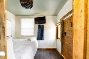 Ein Zimmer mit einem Bett, einem an der Wand befestigten Fernseher und einem Fenster mit Jalousien.