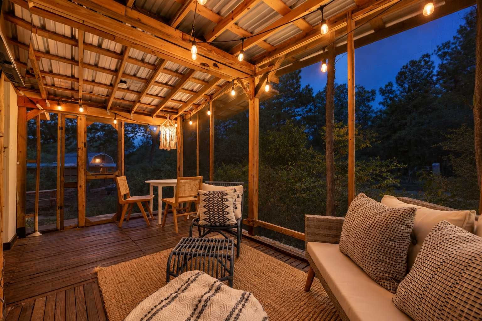 A covered outdoor seating area with wooden furniture, string lights, and a view of the outdoors.