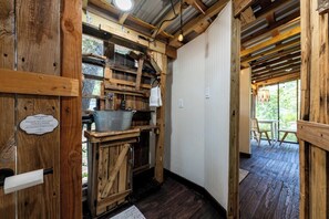 A rustic wooden interior with a wooden toilet, a metal bucket, and a sign instructing to flush only toilet paper. - Pine Lodge Cabin: Open-Air Living in the Pines (Paige)