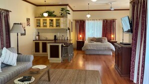 A living room with a sofa, a coffee table, a dining area with a kitchen, a bed, and a TV.