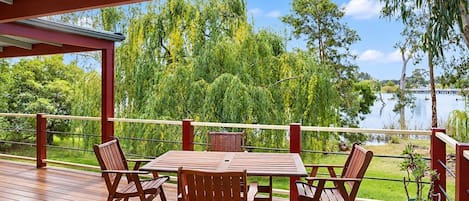 A wooden deck with a table and chairs, overlooking a lake with trees and a clear sky.