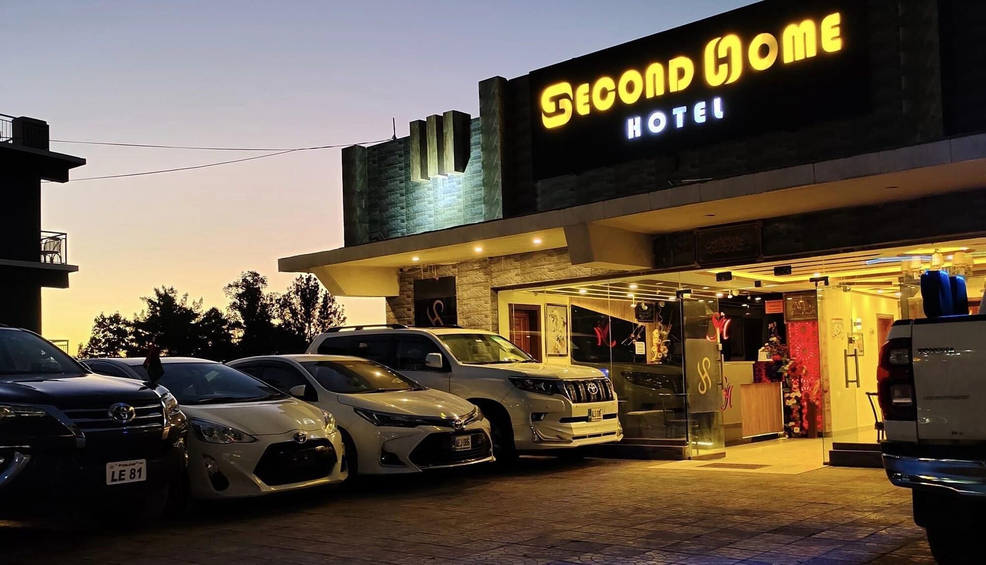 A hotel named 'Second Home' with a modern facade and a parking area with several cars.