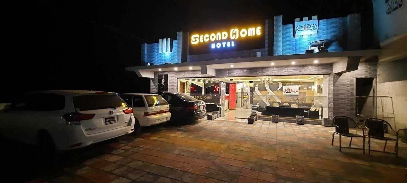 A hotel with a sign reading 'Second Home Hotel' and a parking area with several cars.