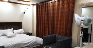 Habitación de hotel con cama, una silla, un ventilador de pared y una cortina.