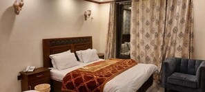 Una habitación de hotel con una cama, una silla, una mesita de noche con un teléfono y una ventana con cortinas.